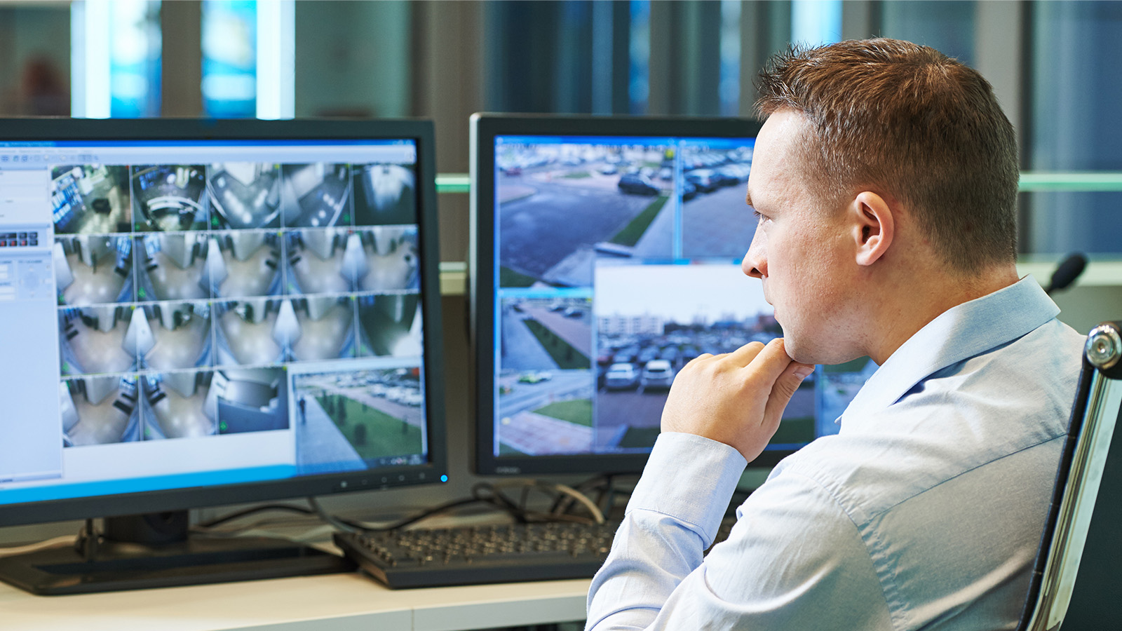 A security manager sitting in front of multiple computer screens with various screenshots of a building.